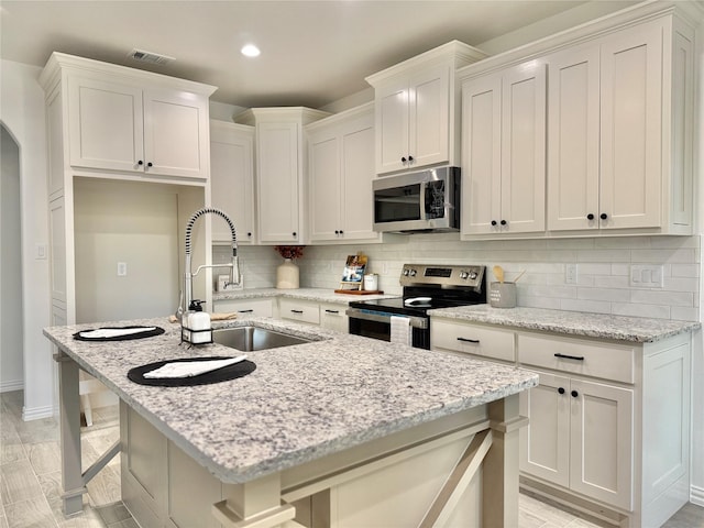 kitchen featuring a kitchen breakfast bar, appliances with stainless steel finishes, sink, light stone countertops, and a center island with sink