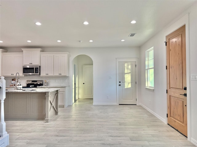 kitchen with stainless steel appliances, white cabinetry, light stone counters, and light hardwood / wood-style flooring