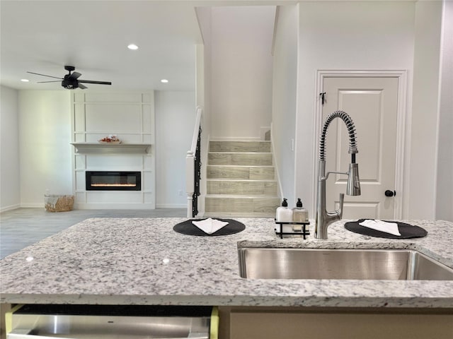 kitchen featuring dishwasher, ceiling fan, sink, light stone countertops, and a fireplace