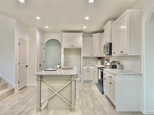 kitchen with light stone countertops, white cabinets, stainless steel appliances, light hardwood / wood-style floors, and a kitchen island with sink