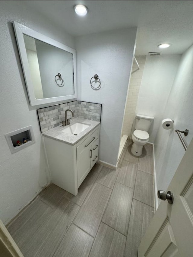 bathroom with tasteful backsplash, vanity, walk in shower, and toilet