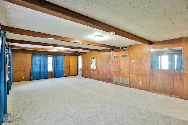 carpeted empty room featuring beamed ceiling and wood walls