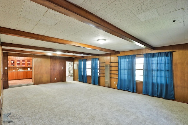 carpeted empty room with beam ceiling and wood walls