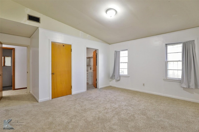 unfurnished bedroom featuring ensuite bathroom, a closet, light carpet, and vaulted ceiling