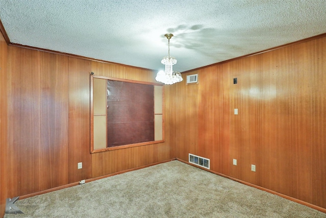 empty room featuring wood walls, light colored carpet, a chandelier, and a textured ceiling