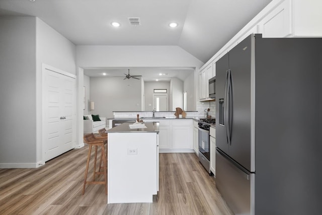 kitchen with a breakfast bar, white cabinets, decorative backsplash, a kitchen island, and stainless steel appliances