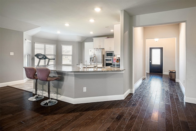 kitchen featuring light stone countertops, stainless steel appliances, a kitchen breakfast bar, dark hardwood / wood-style floors, and white cabinets