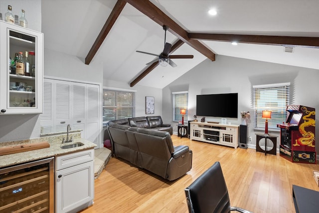 living room with ceiling fan, beverage cooler, wet bar, vaulted ceiling with beams, and light hardwood / wood-style floors