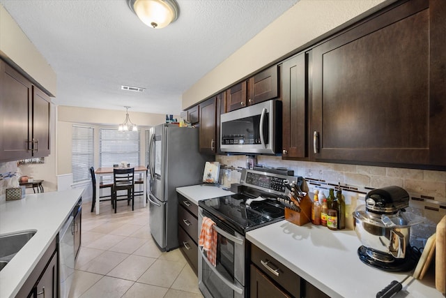 kitchen with decorative backsplash, appliances with stainless steel finishes, dark brown cabinetry, a chandelier, and light tile patterned flooring