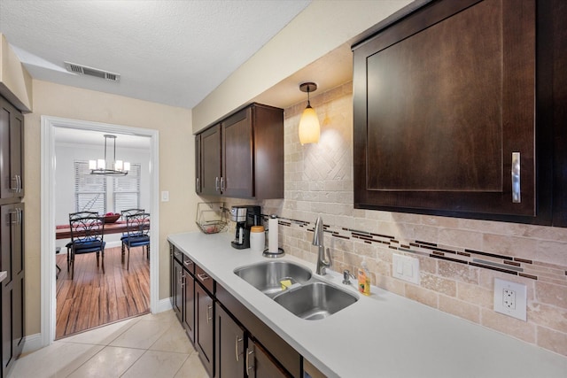 kitchen featuring dark brown cabinetry, sink, light tile patterned floors, and hanging light fixtures