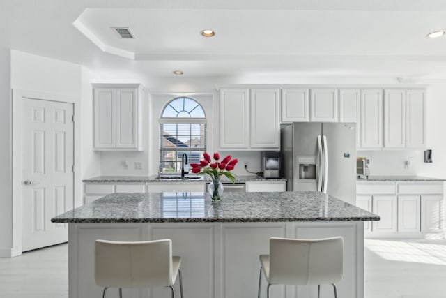 kitchen featuring white cabinetry, sink, a center island, stainless steel refrigerator with ice dispenser, and stone countertops