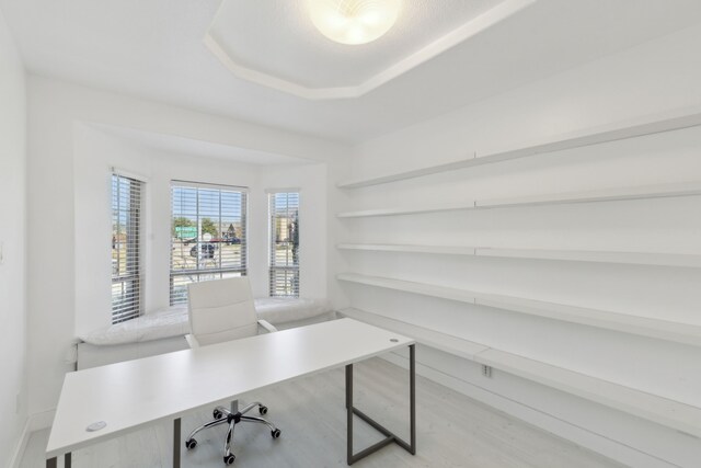 home office with light hardwood / wood-style flooring and a raised ceiling