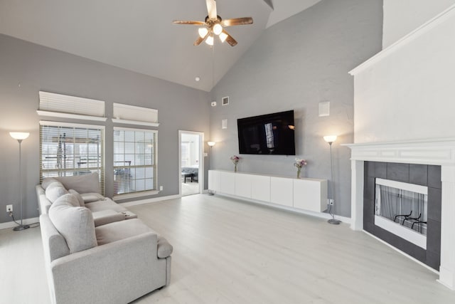 living room with ceiling fan, a fireplace, high vaulted ceiling, and light wood-type flooring