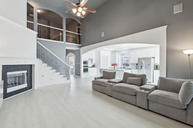 living room featuring ceiling fan, light hardwood / wood-style floors, a towering ceiling, and a fireplace