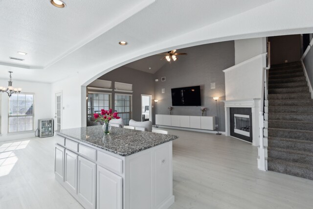 kitchen featuring dark stone counters, ceiling fan with notable chandelier, white cabinets, a center island, and lofted ceiling