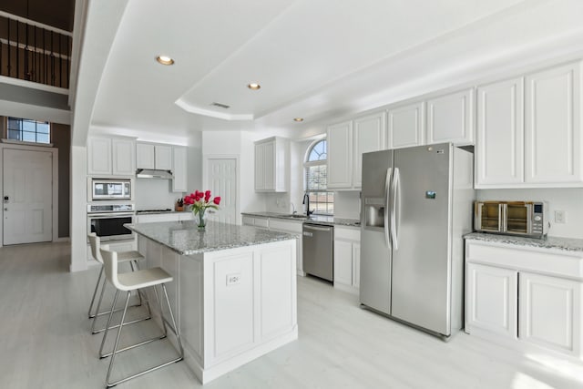 kitchen with white cabinets, a breakfast bar area, a kitchen island, light stone counters, and stainless steel appliances