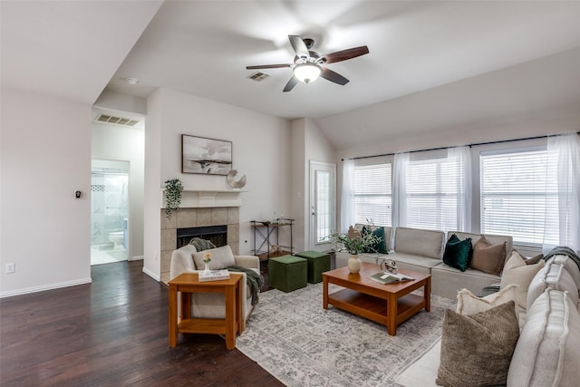 living room featuring a tiled fireplace, a wealth of natural light, ceiling fan, and dark wood-type flooring