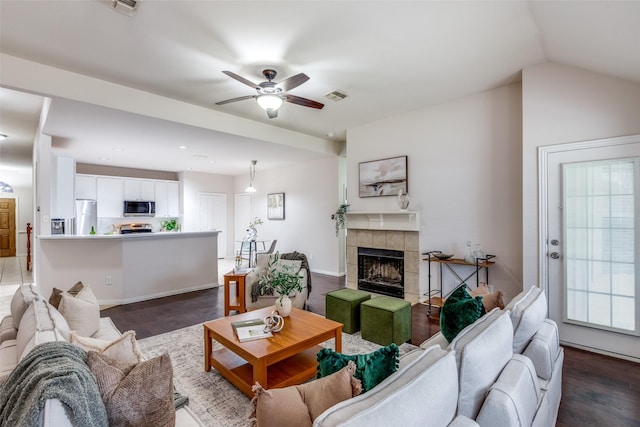 living room with a tile fireplace, dark hardwood / wood-style floors, vaulted ceiling, and ceiling fan