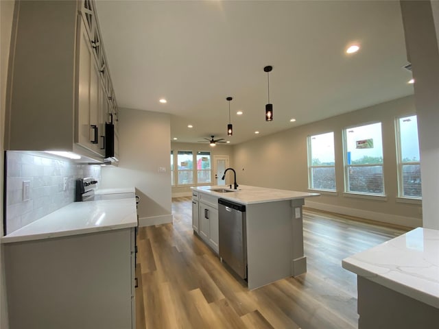 kitchen featuring sink, dishwasher, light stone counters, an island with sink, and decorative light fixtures