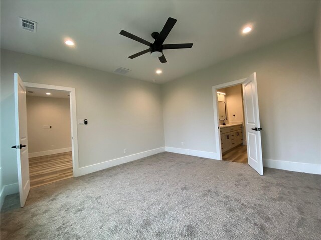 unfurnished bedroom featuring ceiling fan, ensuite bathroom, and dark carpet