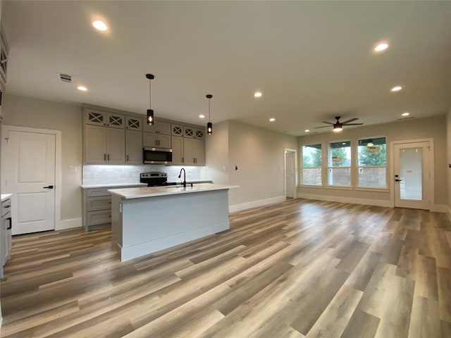 kitchen with appliances with stainless steel finishes, gray cabinetry, a kitchen island with sink, decorative backsplash, and decorative light fixtures