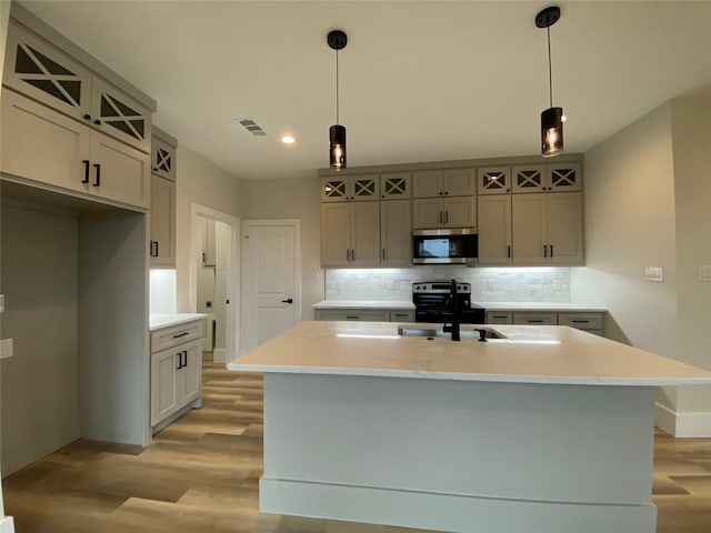 kitchen featuring black / electric stove, tasteful backsplash, decorative light fixtures, and a center island with sink