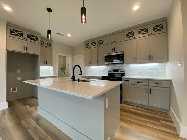 kitchen featuring sink, a kitchen island with sink, hanging light fixtures, electric range oven, and decorative backsplash