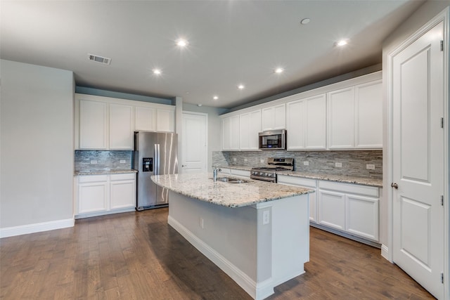 kitchen featuring appliances with stainless steel finishes, light stone counters, sink, white cabinetry, and an island with sink