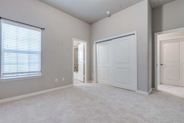 unfurnished bedroom with a closet, light colored carpet, multiple windows, and ensuite bathroom