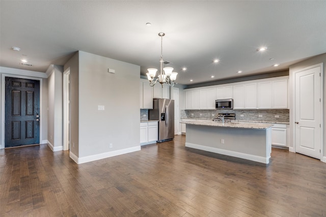 kitchen featuring stainless steel appliances, a notable chandelier, pendant lighting, a kitchen island with sink, and white cabinets