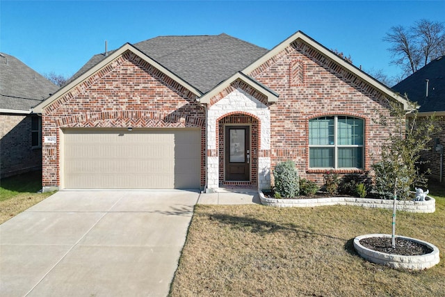 french country inspired facade with brick siding, roof with shingles, concrete driveway, a garage, and a front lawn