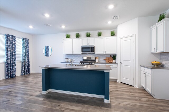 kitchen with sink, stainless steel appliances, white cabinets, a center island with sink, and light wood-type flooring