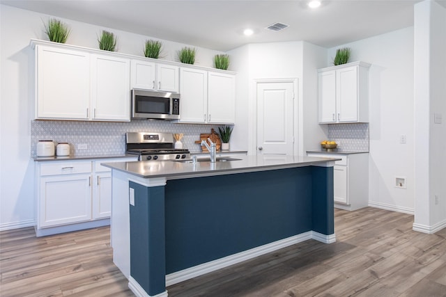 kitchen with sink, stainless steel appliances, white cabinets, a center island with sink, and light wood-type flooring