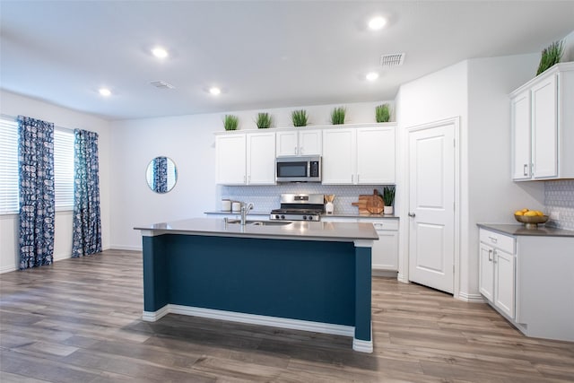 kitchen featuring visible vents, appliances with stainless steel finishes, wood finished floors, white cabinetry, and a sink