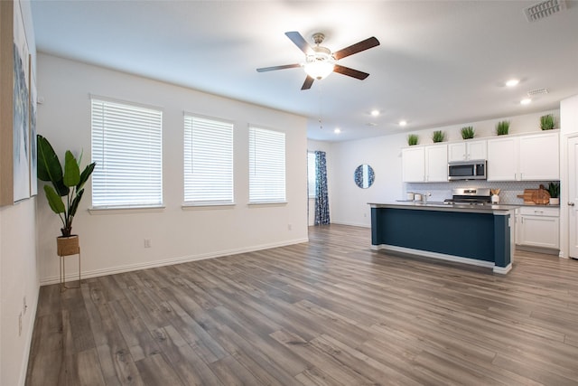 kitchen featuring tasteful backsplash, stainless steel appliances, a kitchen island with sink, hardwood / wood-style flooring, and white cabinetry