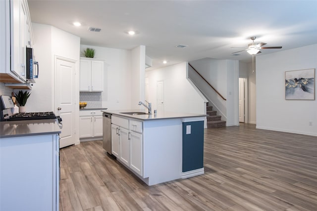 kitchen with a center island with sink, sink, stainless steel dishwasher, tasteful backsplash, and white cabinetry