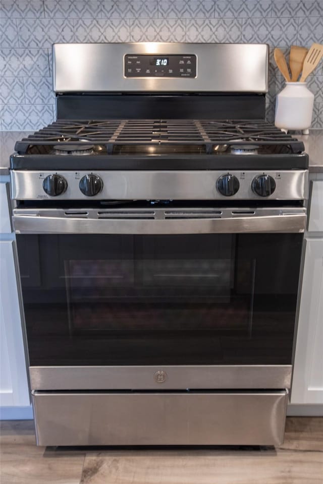 details with backsplash, stainless steel gas range oven, and white cabinetry