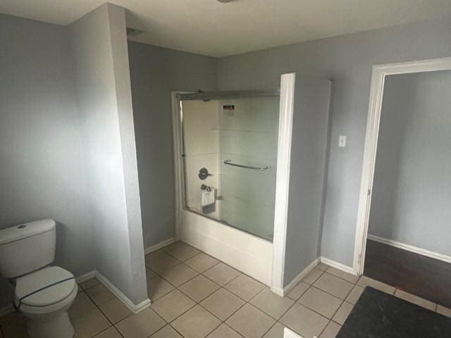 bathroom with tile patterned floors, toilet, and bath / shower combo with glass door