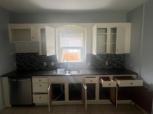 kitchen featuring sink, light tile patterned floors, stainless steel dishwasher, backsplash, and white cabinets