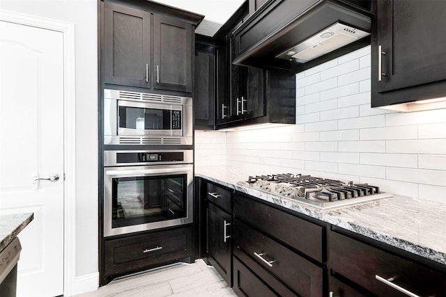 kitchen with light stone countertops, appliances with stainless steel finishes, tasteful backsplash, and wall chimney range hood