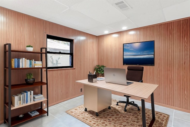 office area with a drop ceiling, light tile patterned floors, and wooden walls