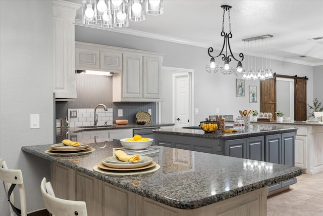 kitchen featuring gray cabinets, a center island, a barn door, decorative light fixtures, and dark stone counters