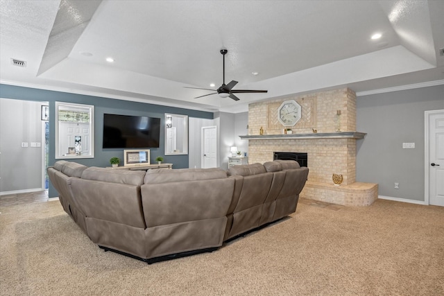 living room featuring a brick fireplace, light colored carpet, and a tray ceiling