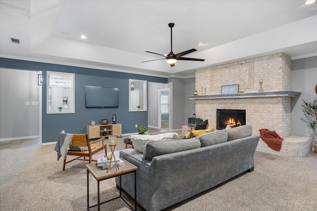 living room with ornamental molding, a tray ceiling, carpet floors, ceiling fan, and a fireplace