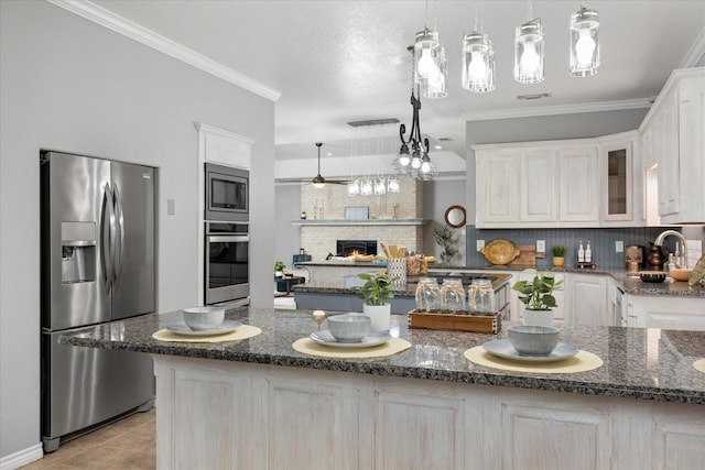 kitchen with ornamental molding, stainless steel appliances, a center island, and dark stone countertops