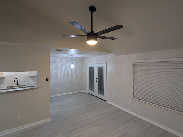 empty room with lofted ceiling, sink, ceiling fan, light hardwood / wood-style floors, and french doors