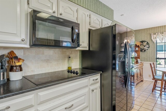 kitchen with a textured ceiling, white cabinets, black appliances, and light tile patterned floors