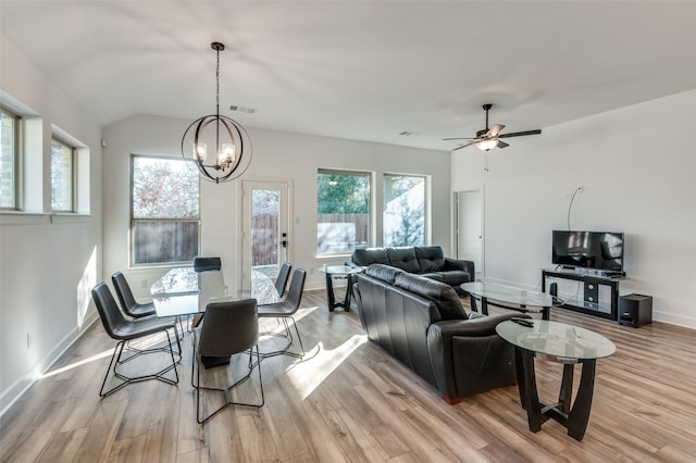 dining area with ceiling fan with notable chandelier, vaulted ceiling, and light wood-type flooring