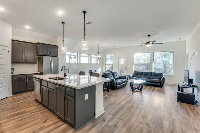 kitchen with appliances with stainless steel finishes, decorative light fixtures, light hardwood / wood-style floors, sink, and a kitchen island with sink