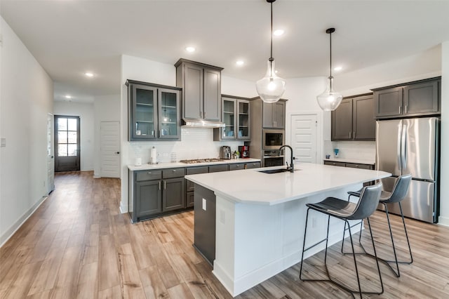 kitchen featuring hanging light fixtures, sink, light wood-type flooring, stainless steel appliances, and a center island with sink